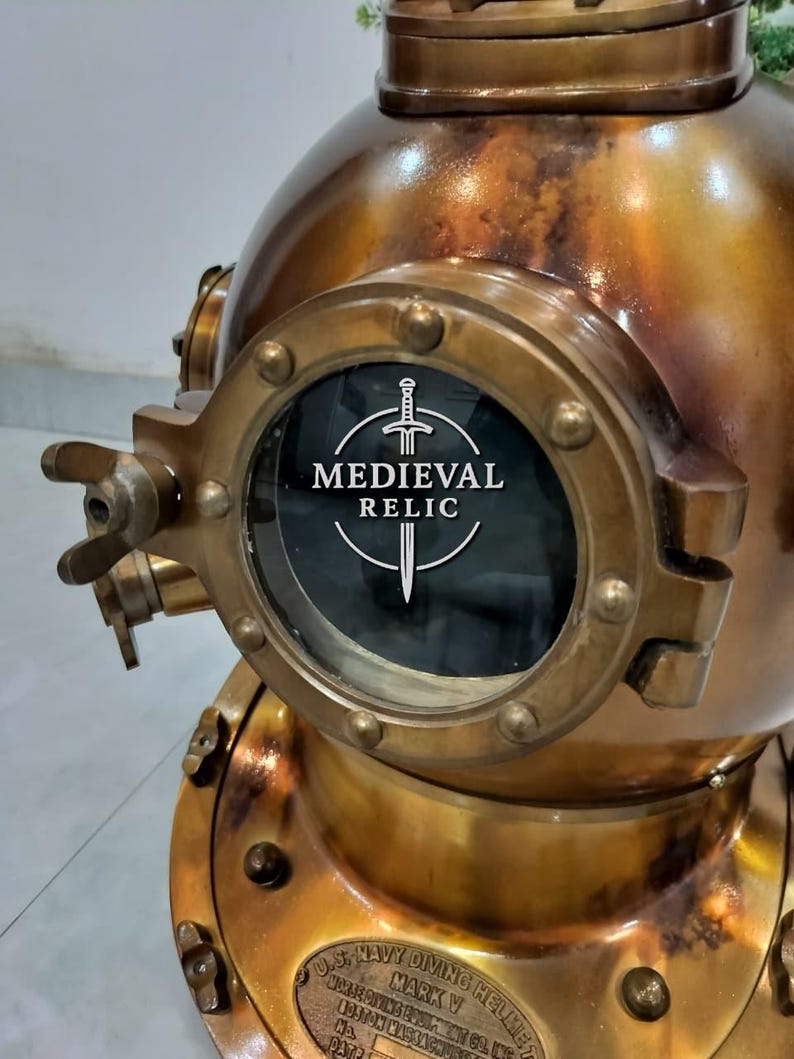 May include: A vintage brass diving helmet with a large circular viewing window. The helmet has a weathered, antique appearance with visible rivets and a plaque that reads "U.S. Navy Diving Helmet". The text "Medieval Relic" is visible on the window.