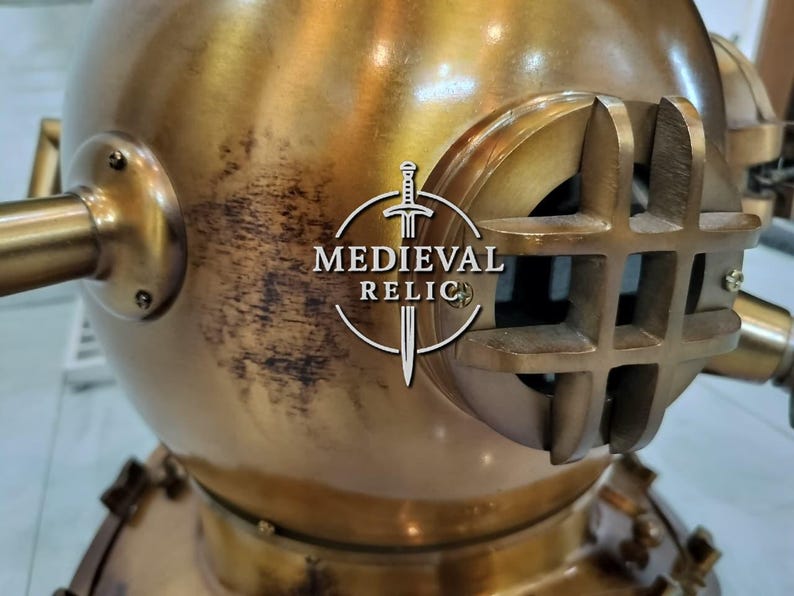 May include: A vintage brass diving helmet with a round body and a large, rectangular viewing window. The helmet has several protruding tubes and fittings, and the text "MEDIEVAL RELIC" is visible on the front.