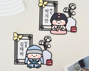 Peut inclure: Deux aimants coréens de personnages de dessins animés. L'un représente une fille en hanbok rose, l'autre un garçon en bleu. Chacun a un nom encadré, un papillon, un vase avec des tiges de coton et une étiquette rouge en forme de cœur.