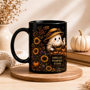 May include: A black ceramic mug featuring a colorful illustration of a ghost wearing a straw hat behind a wooden cart filled with pumpkins. The cart has the text AMELIA'S PUMPKIN STAND printed on it, surrounded by sunflowers and autumn foliage.