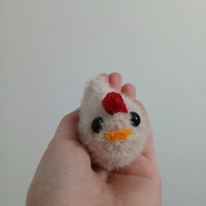 May include: A small white plush chicken toy with red and yellow accents. The chicken has black eyes and a yellow beak.