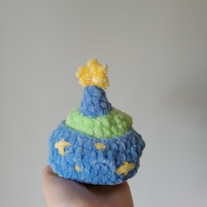 Op de afbeelding: Een blauw en groen gebreid pluche speelgoed in de vorm van een cupcake met een gele ster bovenop.