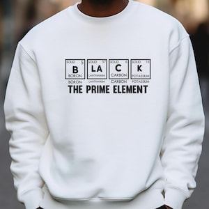 May include: White sweatshirt with the word "BLACK" spelled out using periodic table elements. The text "THE PRIME ELEMENT" is below the word "BLACK". The sweatshirt is a crew neck style.