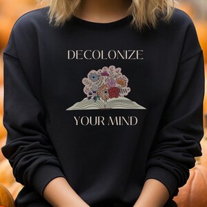 May include: Black sweatshirt with a graphic design of an open book with flowers and the text "DECOLONIZE YOUR MIND".