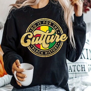 Peut inclure: Sweat-shirt noir avec un graphique circulaire doré qui dit "Do it for the Culture * Black History" avec une bande rouge, jaune et verte au centre.