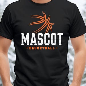 May include: Black t-shirt with an orange basketball graphic and the word "MASCOT" in white block letters. Below the word "MASCOT" is the text "- BASKETBALL -" in orange. The shirt is a crew neck style.