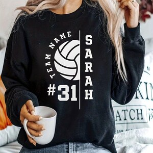 Puede incluir: Sudadera negra con un gráfico de voleibol blanco, el texto "TEAM NAME #31" y el nombre "SARAH" verticalmente en el lado derecho.