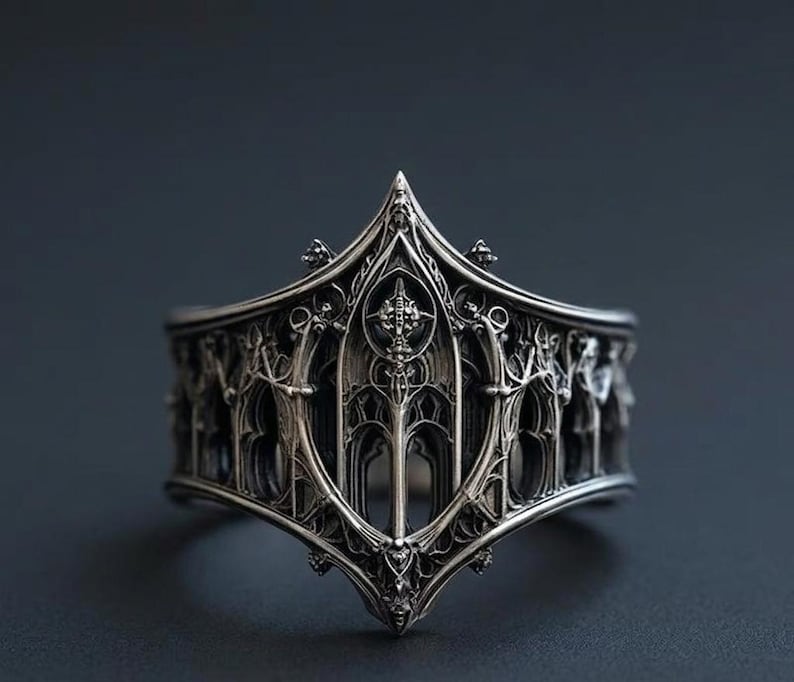 May include: A silver ring featuring an intricate, raised architectural design that mimics pointed arches and vertical columns. The metal has a dark, oxidized finish in the recessed areas, highlighting the detailed, repeating structural patterns.