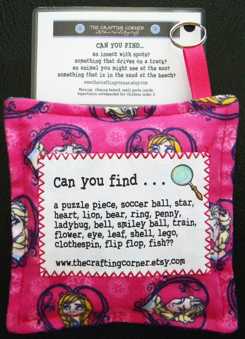 May include: Pink fabric pouch with a white tag that says "Can you find..." and lists a variety of items. The pouch has a pink ribbon attached to it and a clear plastic card with the text "The Crafting Corner" and "Can you find..." with a list of items.