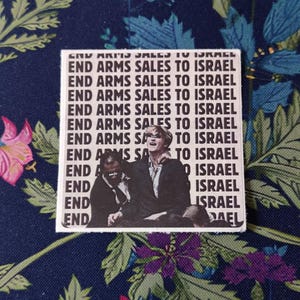 May include: A square sticker with the repeated text "END ARMS SALES TO ISRAEL". The sticker features a black and white image of two people. The background is a dark blue floral pattern with green and pink flowers.