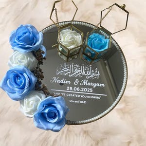 May include: A round mirrored wedding tray decorated with blue and white roses, two hexagonal glass boxes with roses, and gold detailing. The tray features the names "Nadim & Maryam" and the date 29.06.2025, along with a Quran quote.