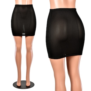 May include: A black, ribbed mini skirt. The skirt is displayed on a mannequin, showcasing its form-fitting design. The fabric has vertical lines, adding texture to the garment. The skirt is a solid black color.