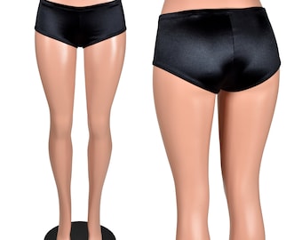 Puede incluir: Shorts de satén negro exhibidos en un maniquí. Los shorts tienen una cintura baja y una textura suave y brillante. La imagen muestra las vistas delantera y trasera de los shorts.