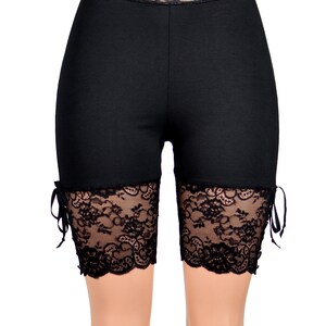 May include: Black biker shorts with a lace trim around the waist and at the bottom of the legs. The lace has a floral pattern.