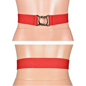 Könnte beinhalten: Ein roter elastischer Gürtel mit einer silberfarbenen Doppelschließe. Der Gürtel wird von vorne und hinten gezeigt, was sein schlichtes Design und das dehnbare Material hervorhebt. Dieses Accessoire ist für verschiedene Outfits geeignet.