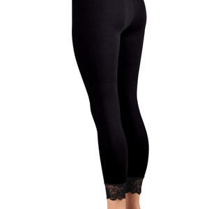 May include: Black leggings with a black lace waistband and trim at the ankles. The leggings are on a mannequin with nude legs and are standing on a black circular base.