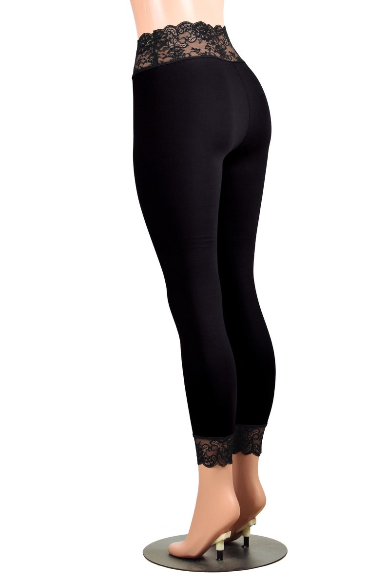 May include: Black leggings with a black lace waistband and trim at the ankles. The leggings are on a mannequin with nude legs and are standing on a black circular base.