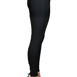 Op de afbeelding: Zwarte leggings met een vetersluiting aan de zijkant van elk been.
