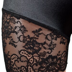 May include: A pair of black shorts featuring a smooth, slightly reflective fabric upper section and a wide, intricate black floral lace trim along the bottom edge. The lace has a scalloped hemline and a detailed, open-work botanical pattern.