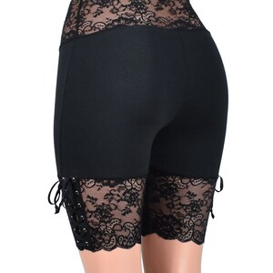 May include: Black high-waisted shorts with black lace trim around the waistband and at the bottom of the legs. The lace has a scalloped edge and is tied at the sides.