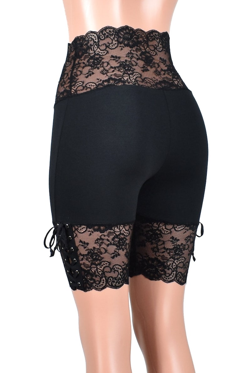 May include: Black high-waisted shorts with black lace trim around the waistband and at the bottom of the legs. The lace has a scalloped edge and is tied at the sides.