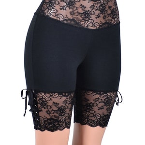 May include: Black biker shorts with lace trim at the waist and legs. The lace trim has a floral pattern and is tied at the sides.
