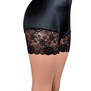 May include: High-waisted black satin shorts featuring a smooth, solid fabric finish on the upper portion and a wide band of intricate black floral lace trim along the bottom hem, providing a structured fit with a clean, finished edge design.
