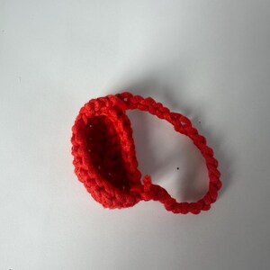 Puede incluir: Un art&iacute;culo de ganchillo rojo brillante hecho a mano, posiblemente una peque&ntilde;a cesta o contenedor. El art&iacute;culo est&aacute; hecho de hilo grueso y tiene una apariencia texturizada. La forma es ovalada con un asa en bucle. El fondo es blanco liso.