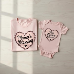 Op de afbeelding: Twee bijpassende roze kledingstukken. Eén is een t-shirt met de tekst "Mama's Blessing" in een hartvormig ontwerp. De andere is een babyromper met de tekst "Tiny Blessing Valentine" in een hartvormig ontwerp.