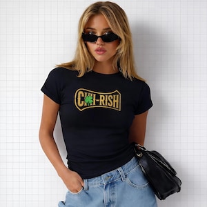 May include: Black t-shirt with the text "CHI-RISH" in a gold and green design. The shirt features a shamrock graphic. The t-shirt is a crew neck style.