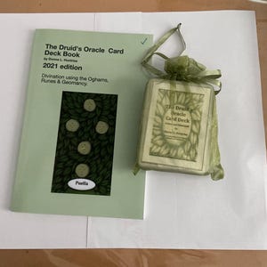 May include: A light green book and card deck set titled "The Druid's Oracle Card Deck Book" by Donna L. Hunt, 2021 edition. The book cover features a green and white design. The card deck is in a green mesh bag.