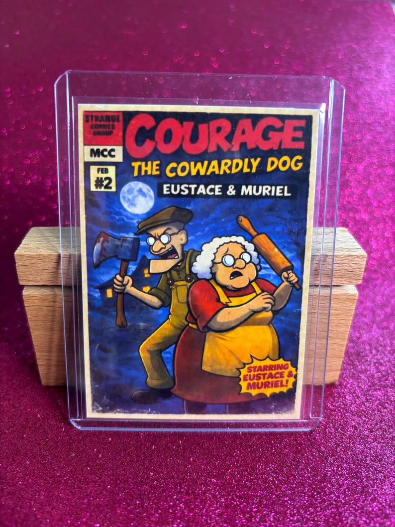 May include: A Courage the Cowardly Dog trading card, featuring Eustace and Muriel. The card has a red and yellow title with the text "COURAGE THE COWARDLY DOG". Eustace holds an axe, and Muriel holds a rolling pin. The card is in a protective sleeve.
