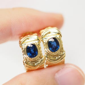 May include: A pair of gold hoop earrings with a blue sapphire gemstone in each hoop.