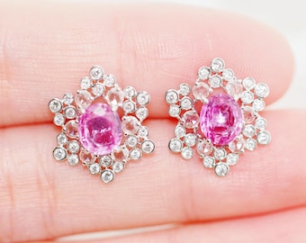 May include: A pair of silver earrings with a pink gemstone surrounded by smaller white gemstones in a starburst design.