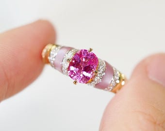 Può includere: Un anello in oro bianco con una pietra ovale rosa e accenti di smalto rosa. L'anello è incastonato con piccoli diamanti attorno alla pietra preziosa.