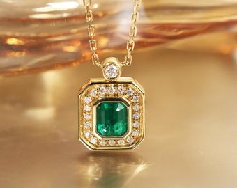 May include: A gold necklace with a rectangular pendant featuring a vibrant green emerald center stone. The emerald is surrounded by a halo of small, sparkling diamonds. A single diamond accents the chain's connection to the pendant.