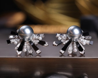 May include: A pair of silver earrings with black and white accents. Each earring features a large grey pearl surrounded by a cluster of smaller white pearls and black geometric shapes.