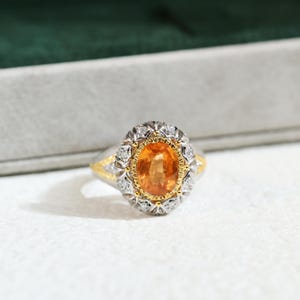 Pode incluir: Um anel de ouro e prata com uma grande gema laranja cercada por diamantes menores.