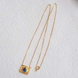 May include: A gold chain necklace with a pendant featuring a blue gemstone set in a textured gold frame.