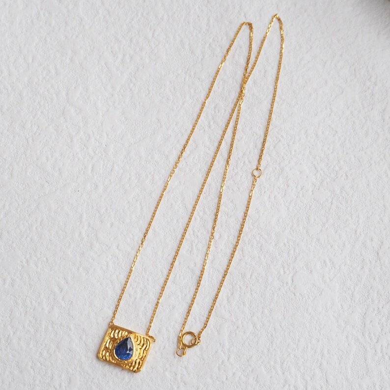 May include: A gold chain necklace with a pendant featuring a blue gemstone set in a textured gold frame.