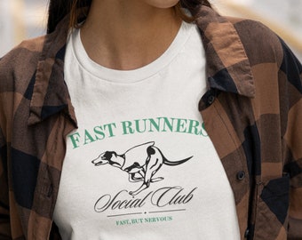 May include: White t-shirt with a black and white illustration of a dog running. The text "FAST RUNNERS Social Club FAST, BUT NERVOUS" is printed on the shirt in green.