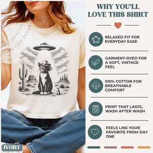K&ouml;nnte beinhalten: Ein elfenbeinfarbenes T-Shirt mit einer schwarzen Grafik, die eine Katze mit Cowboyhut unter einem UFO in einer W&uuml;stenlandschaft mit Kaktus und kleiner Maus zeigt. Rechts steht der Text: WHY YOU'LL LOVE THIS SHIRT, RELAXED FIT, 100% COTTON.