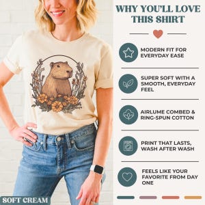May include: A soft cream-colored t-shirt featuring a capybara illustration surrounded by flowers. The shirt has the text "WHY YOU'LL LOVE THIS SHIRT" and bullet points describing the shirt's features, including a modern fit, soft feel, and durable print.
