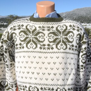 May include: A white and green knitted jumper with a traditional Scandinavian pattern. The jumper has a crew neck and long sleeves.