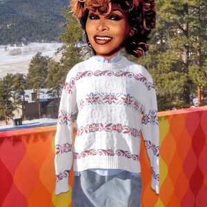 May include: White sweater with a red, blue, and white geometric pattern. The sweater has long sleeves and a crew neck.