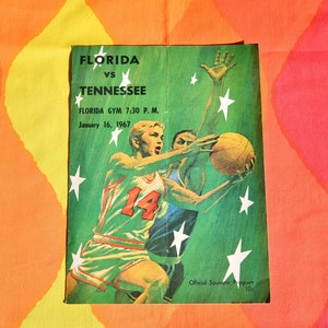 May include: A vintage program for a basketball game between the University of Florida and the University of Tennessee. The program features a green background with white stars and a drawing of two basketball players in action. The text on the program reads "Florida vs Tennessee, Florida Gym 7:30 P.M., January 16, 1967, Official Souvenir Program 10c."