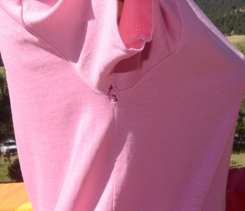 May include: A pink t-shirt with a small tear in the shoulder seam.