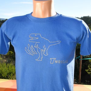 May include: A blue t-shirt featuring a rhinestone design of a dinosaur and the word "Twrecks" in white. The short-sleeved shirt is displayed on a mannequin.