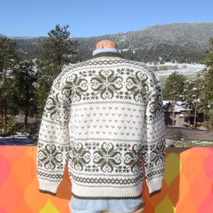 May include: White and green knitted sweater with a traditional Scandinavian pattern. The sweater has a crew neck and long sleeves.