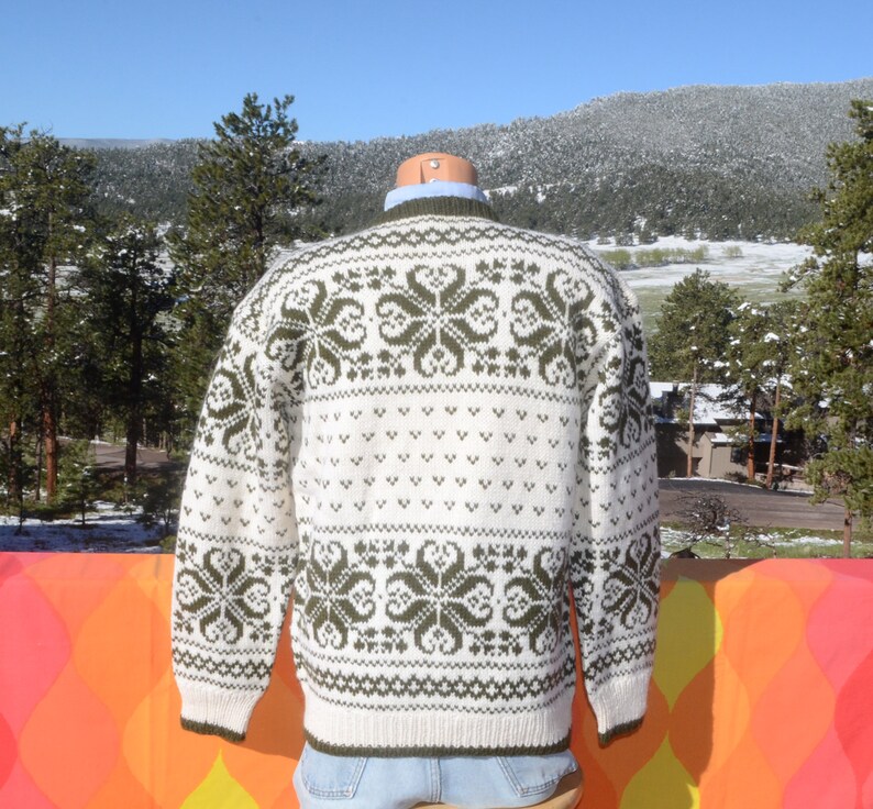 May include: White and green knitted sweater with a traditional Scandinavian pattern. The sweater has a crew neck and long sleeves.